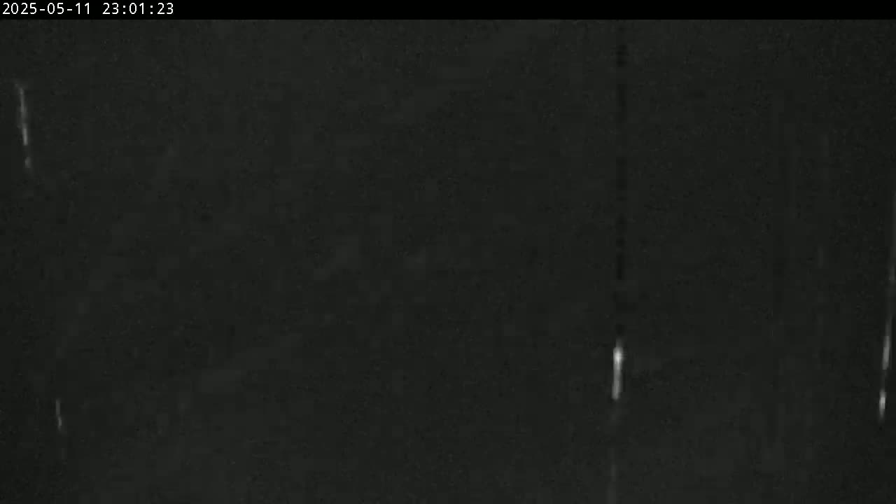 A nighttime outdoor scene shows a dark, possibly overcast sky with faint streaks of light suggesting rain or snow.