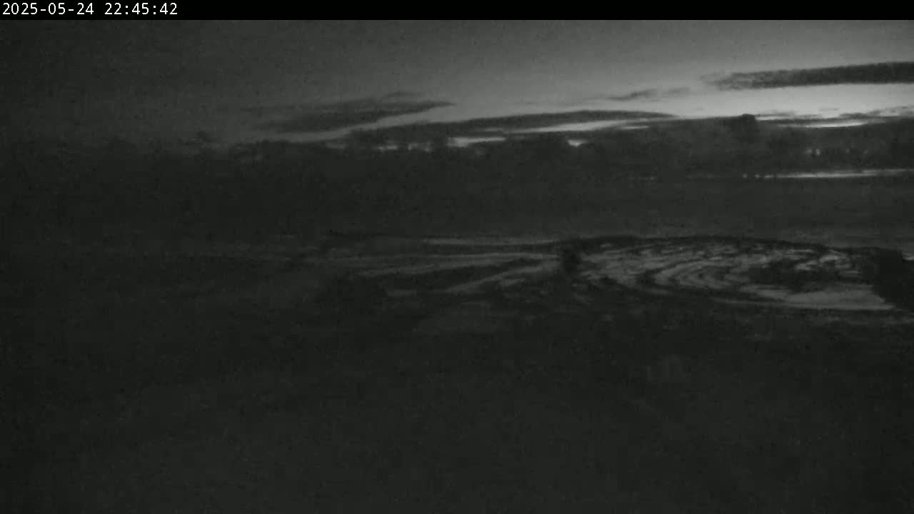 A dark, low-light outdoor scene shows a flat, dark landscape under a mostly clear, twilight sky.