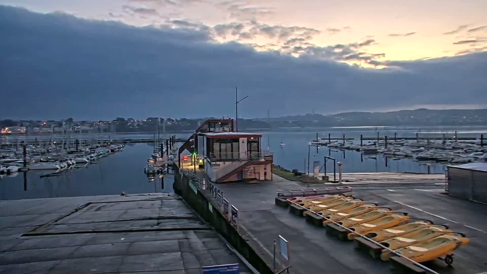 A marina with numerous boats at a calm harbor under a cloudy, sunrise sky.