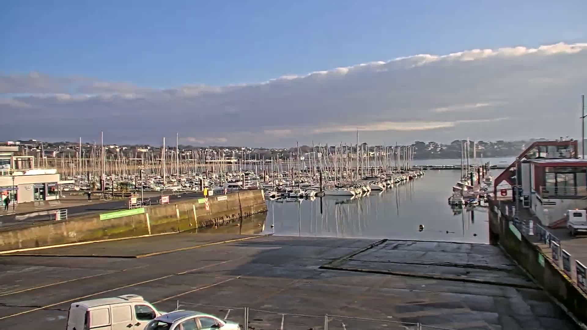 A marina filled with numerous sailboats under a mostly clear sky with a band of clouds.