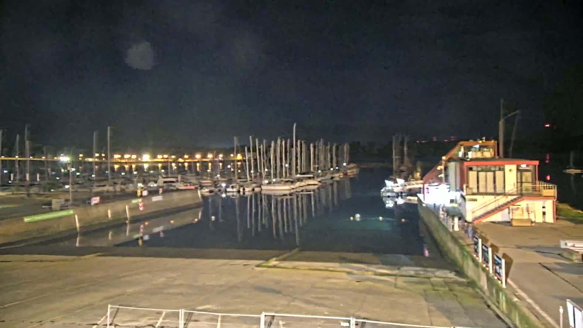 At night, a marina filled with sailboats is calm under a dark sky.
