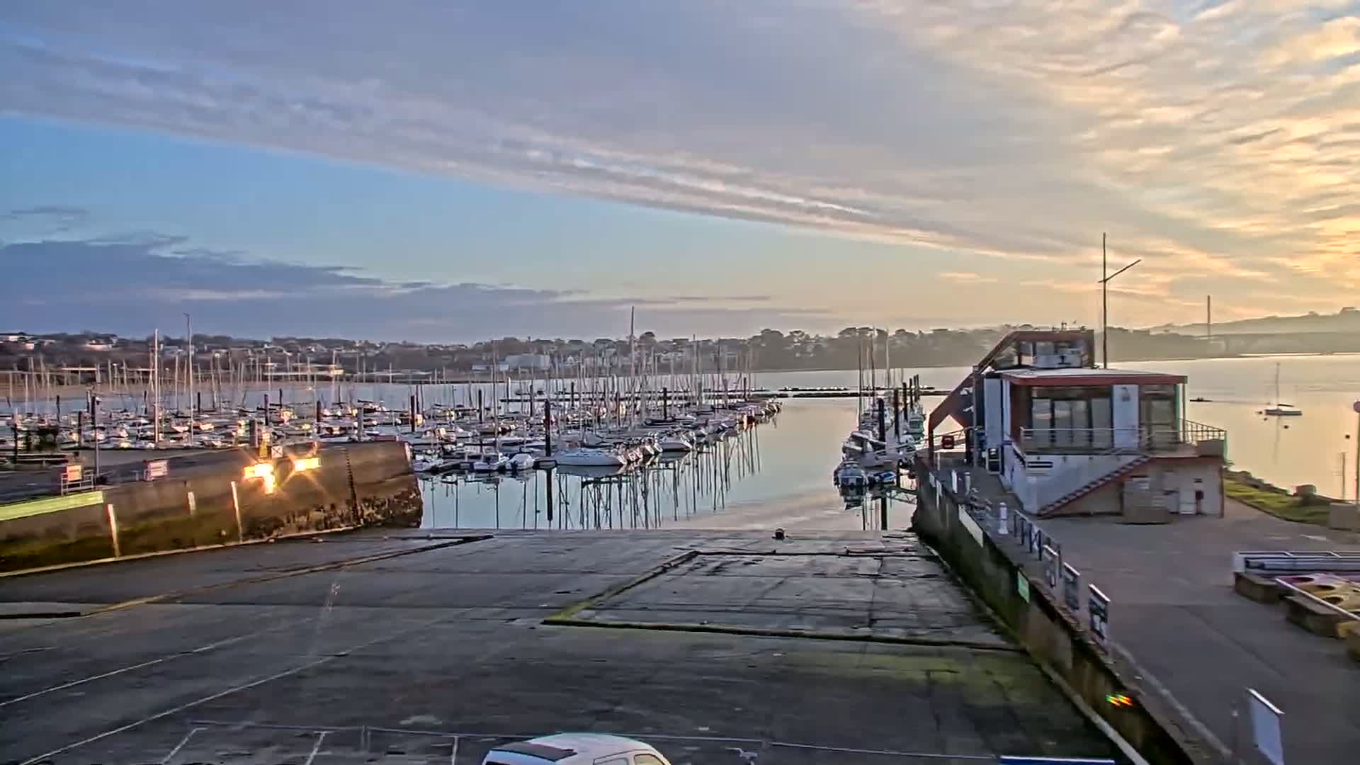 A marina filled with sailboats is seen at sunrise under a mostly clear sky.