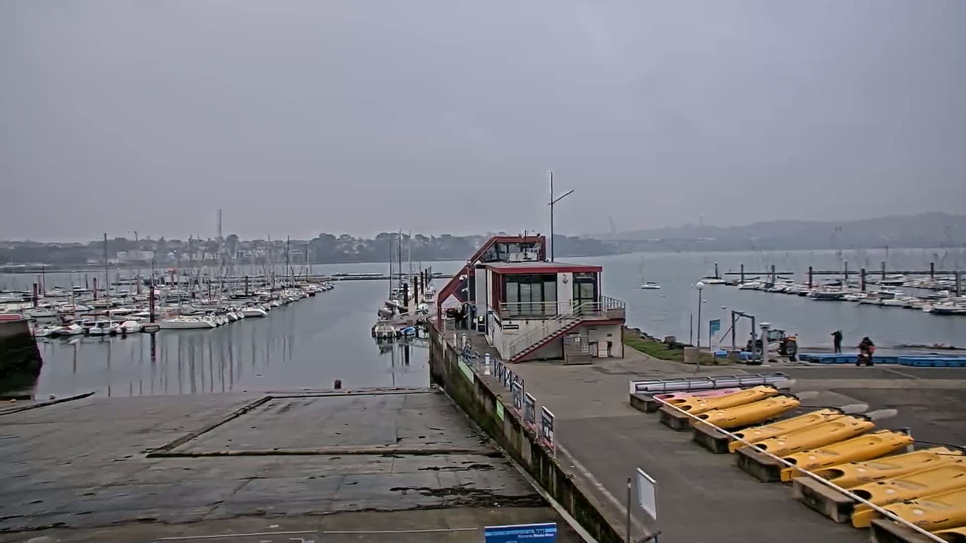 A marina filled with sailboats on a hazy day, with a small building and kayaks visible in the foreground.