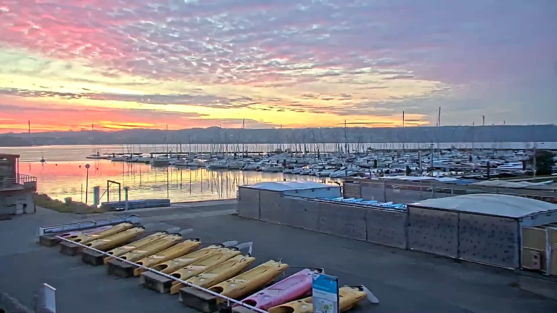 A calm marina filled with numerous boats at sunrise under a colorful, partly cloudy sky.