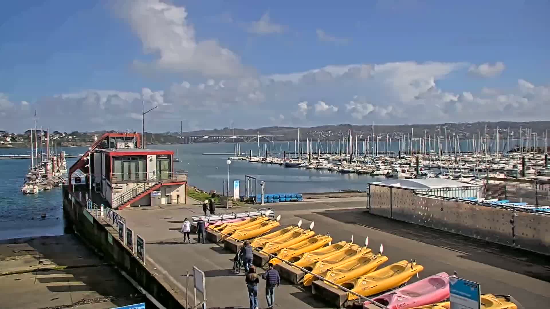 A marina with numerous boats and kayaks, under a partly cloudy sky.