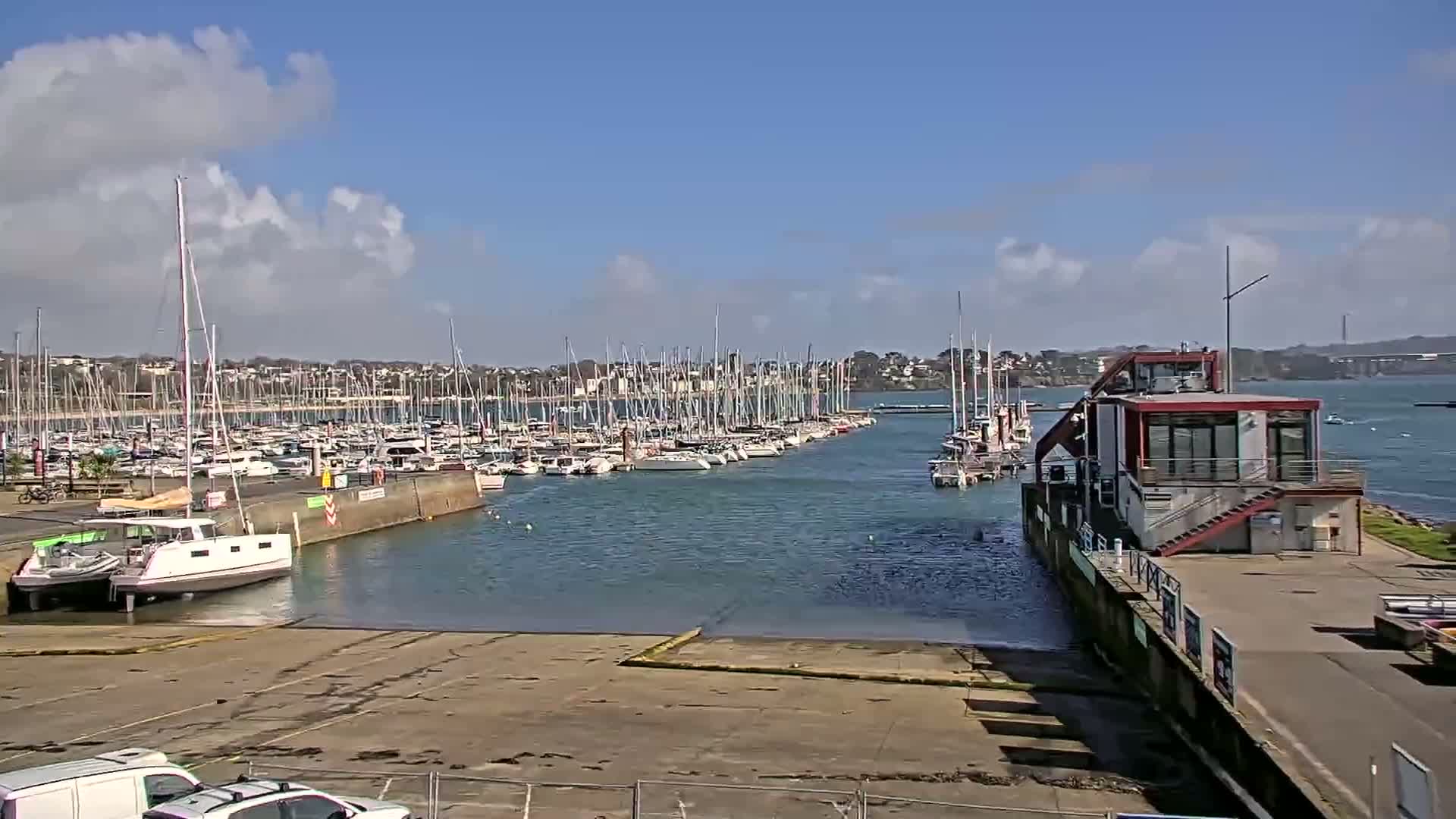 A marina filled with sailboats is seen under a partly sunny sky.