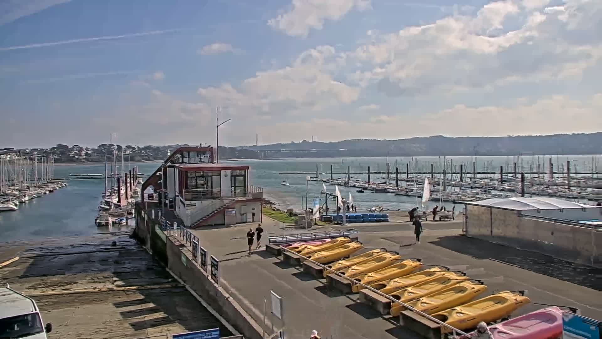 A marina with numerous sailboats and kayaks on a partly sunny day.