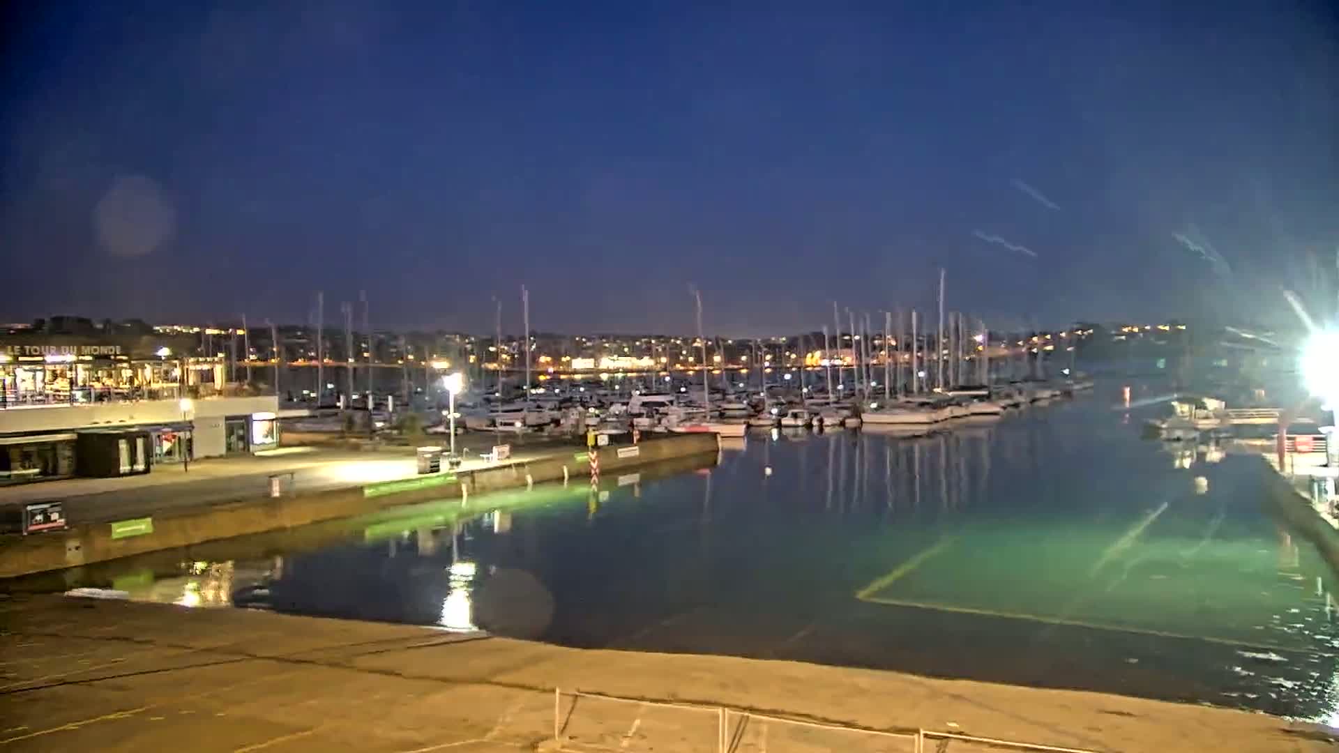 A marina at night, filled with numerous sailboats, under a clear, dark blue sky.