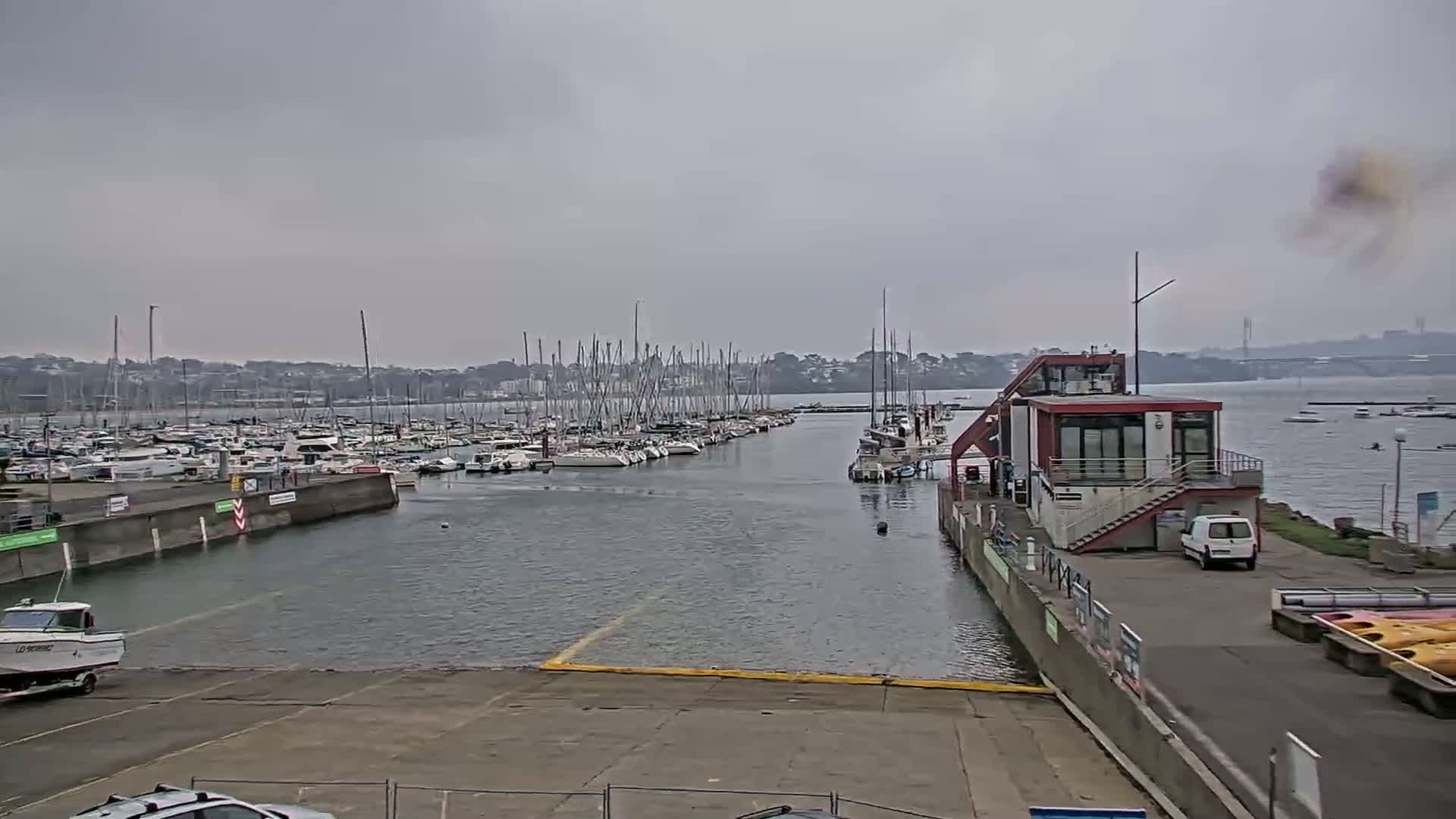 A marina filled with numerous sailboats under an overcast sky, with a small building and a few other vehicles visible nearby.