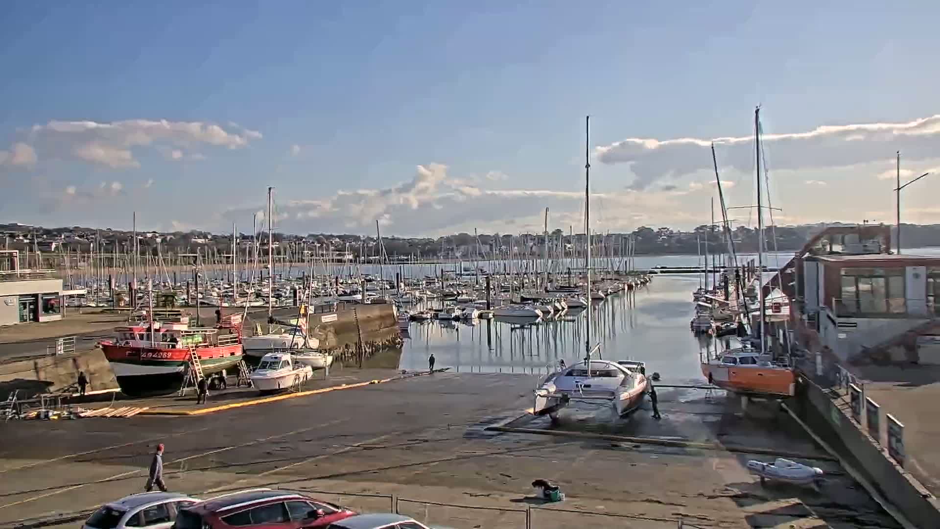 A marina filled with sailboats and motorboats under a partly cloudy blue sky.