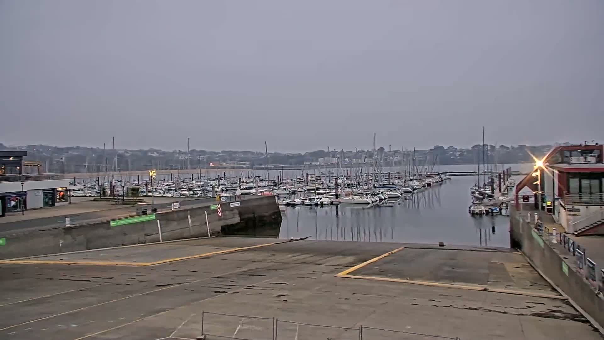 A marina filled with sailboats is viewed from a boat ramp on an overcast day.