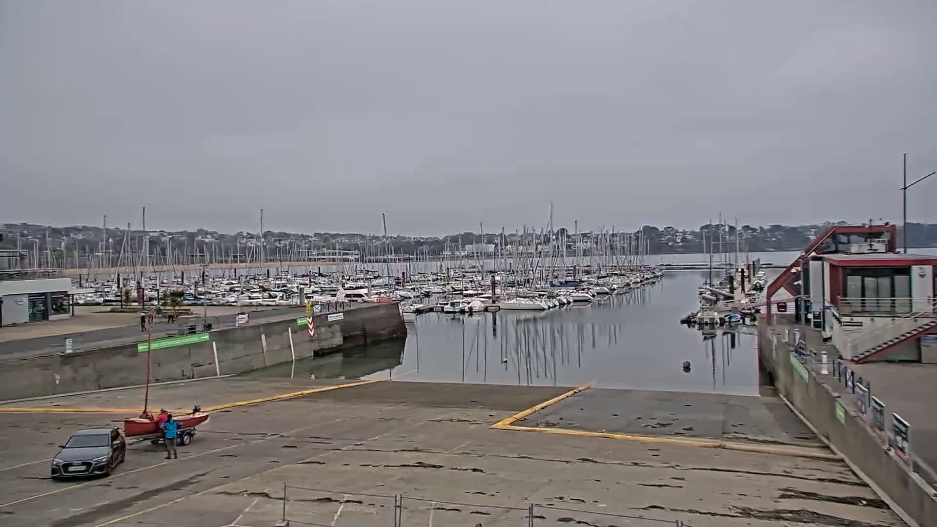 A marina filled with numerous sailboats under an overcast sky, with a small boat being launched from a ramp.