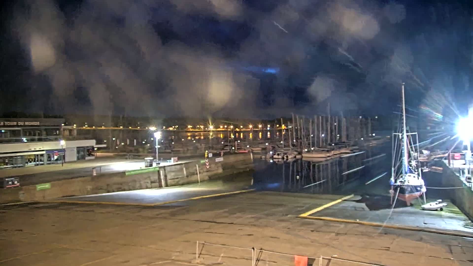 A nighttime view of a harbor with many boats docked, under a cloudy sky.