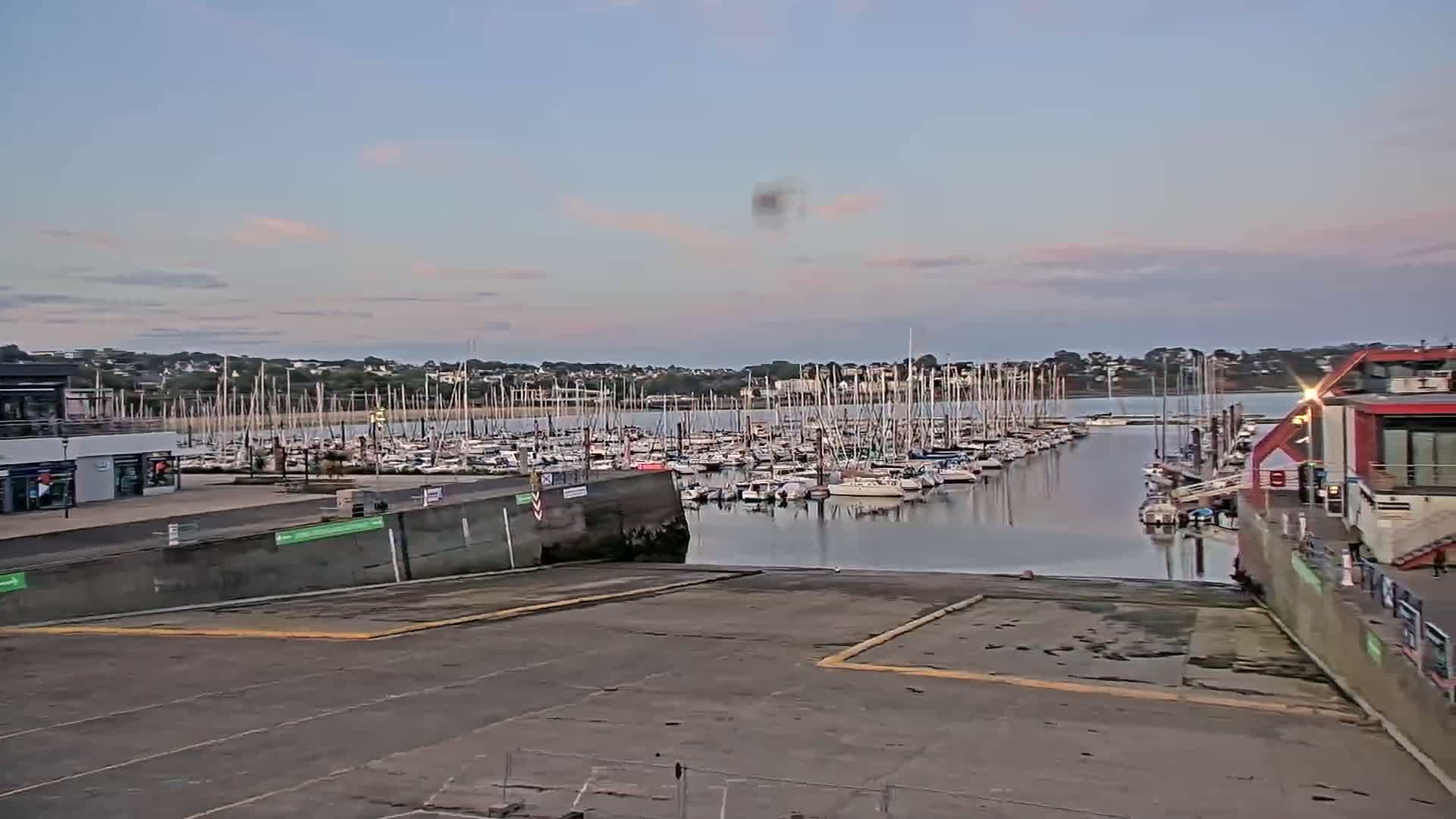 A marina filled with sailboats under a partly cloudy, twilight sky.
