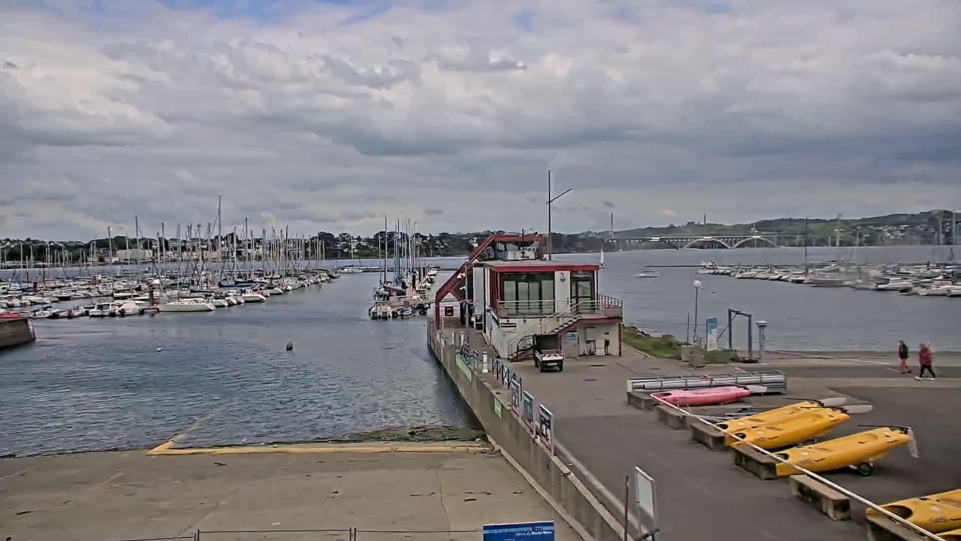 A marina filled with sailboats under a cloudy sky, with a small building and kayaks on the land.