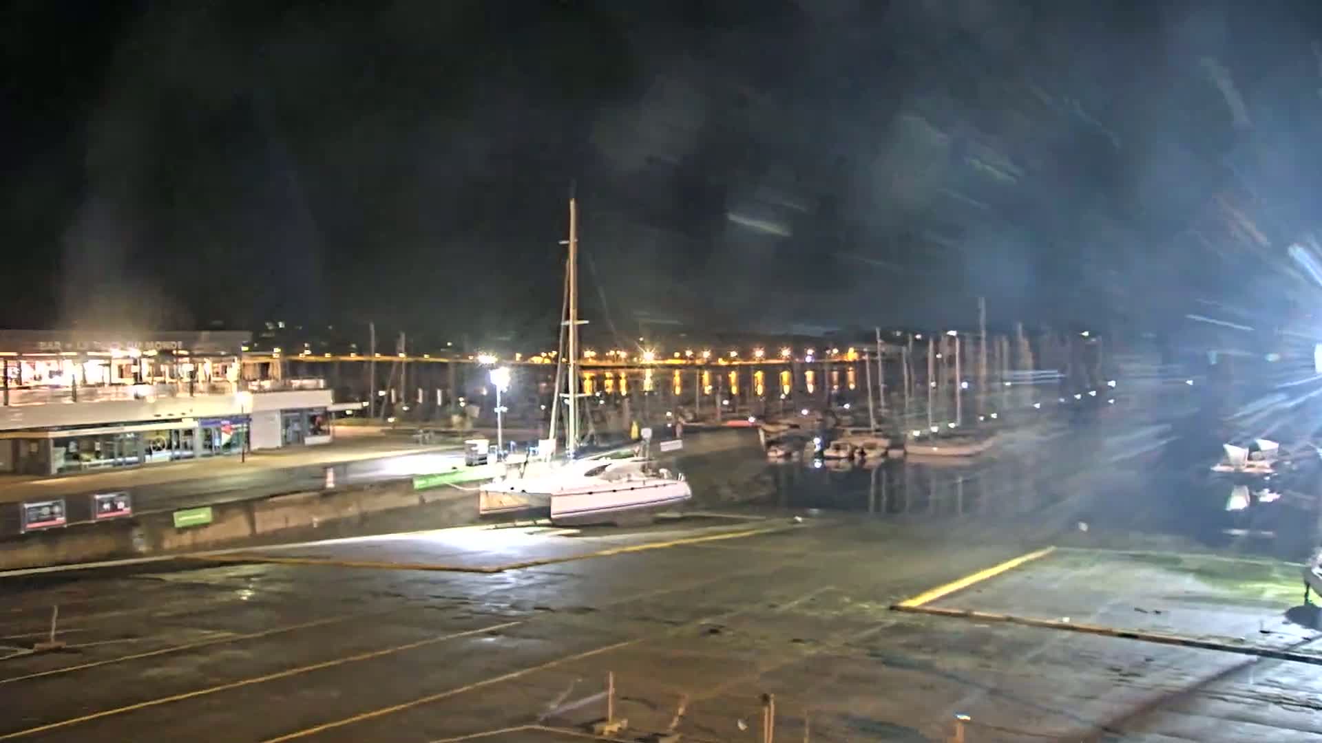 A catamaran is docked at night in a marina, under a dark and hazy sky.