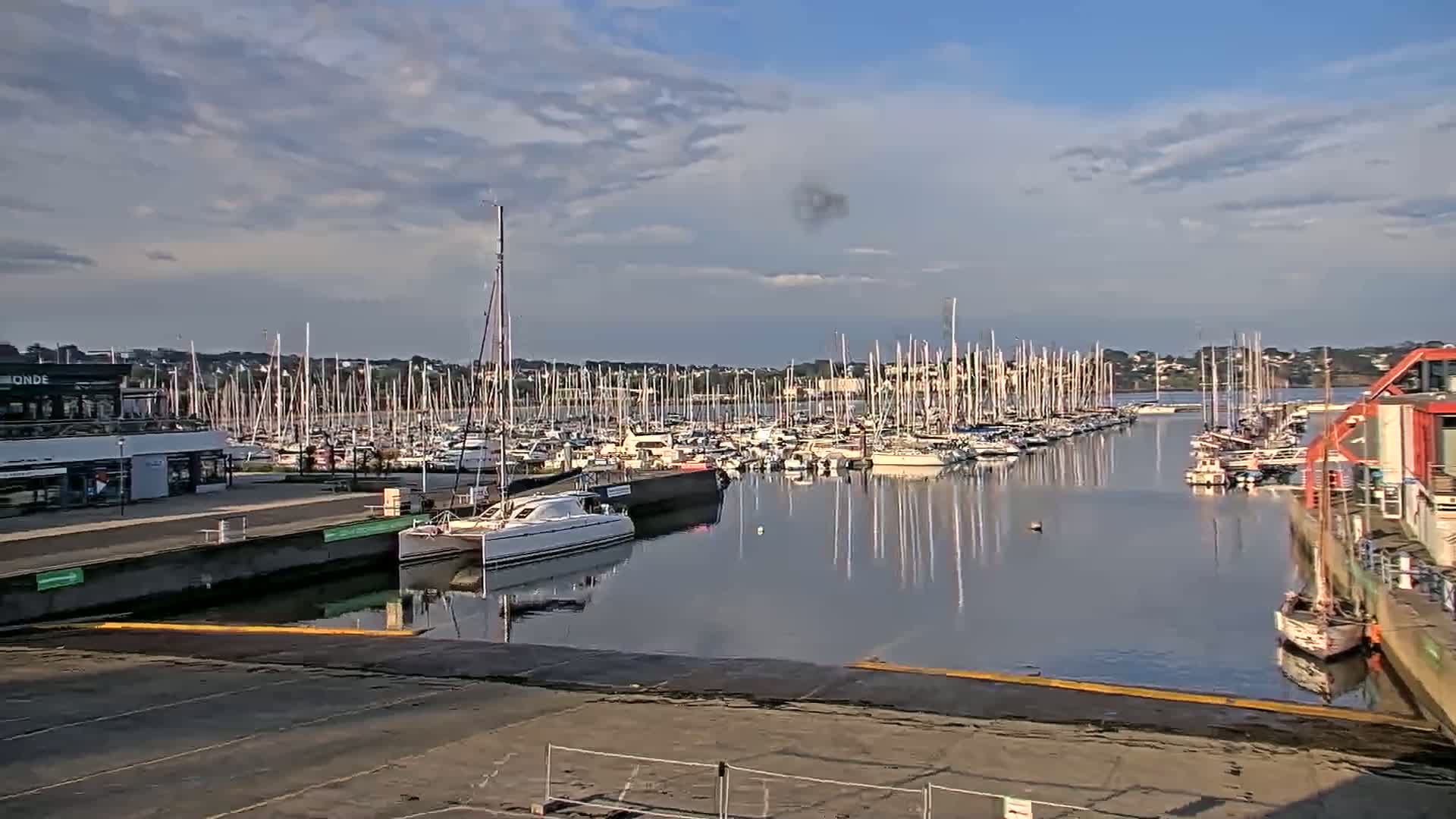A calm marina filled with numerous sailboats and motorboats under a partly cloudy sky.