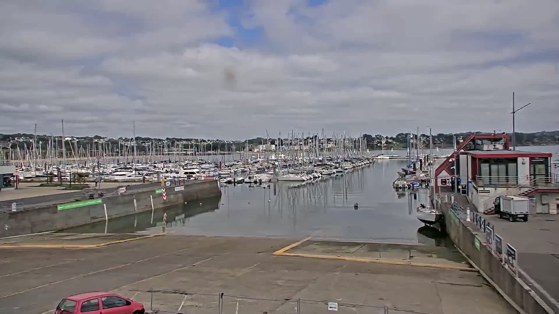 A marina filled with numerous sailboats under a cloudy sky, viewed from a boat ramp.