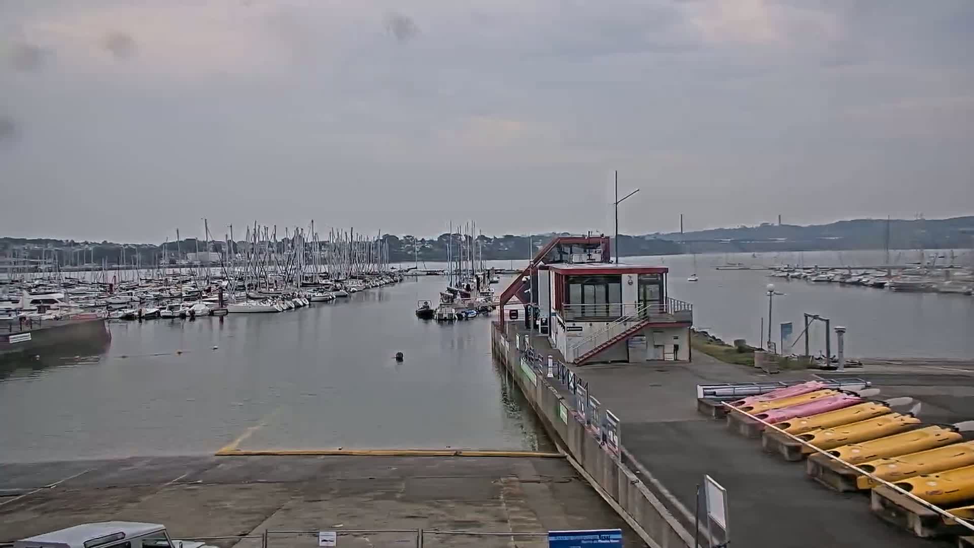 A marina filled with sailboats under an overcast sky, with a small building and several kayaks nearby.