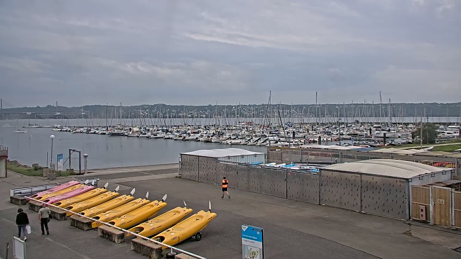 A marina filled with sailboats under a cloudy sky, with kayaks and canoes lined up on the shore.