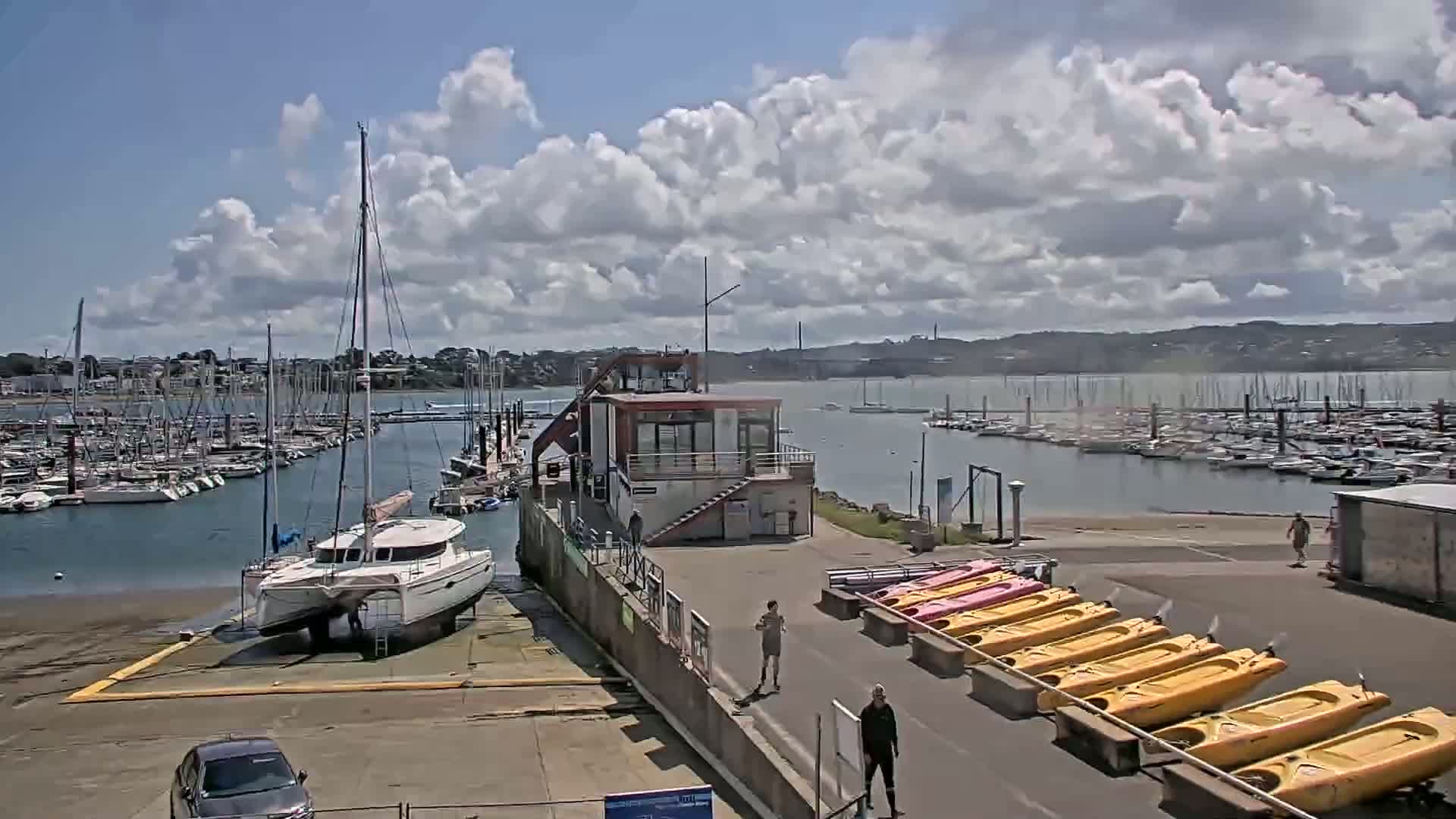 A marina with numerous sailboats and a catamaran on land, under a partly cloudy sky.