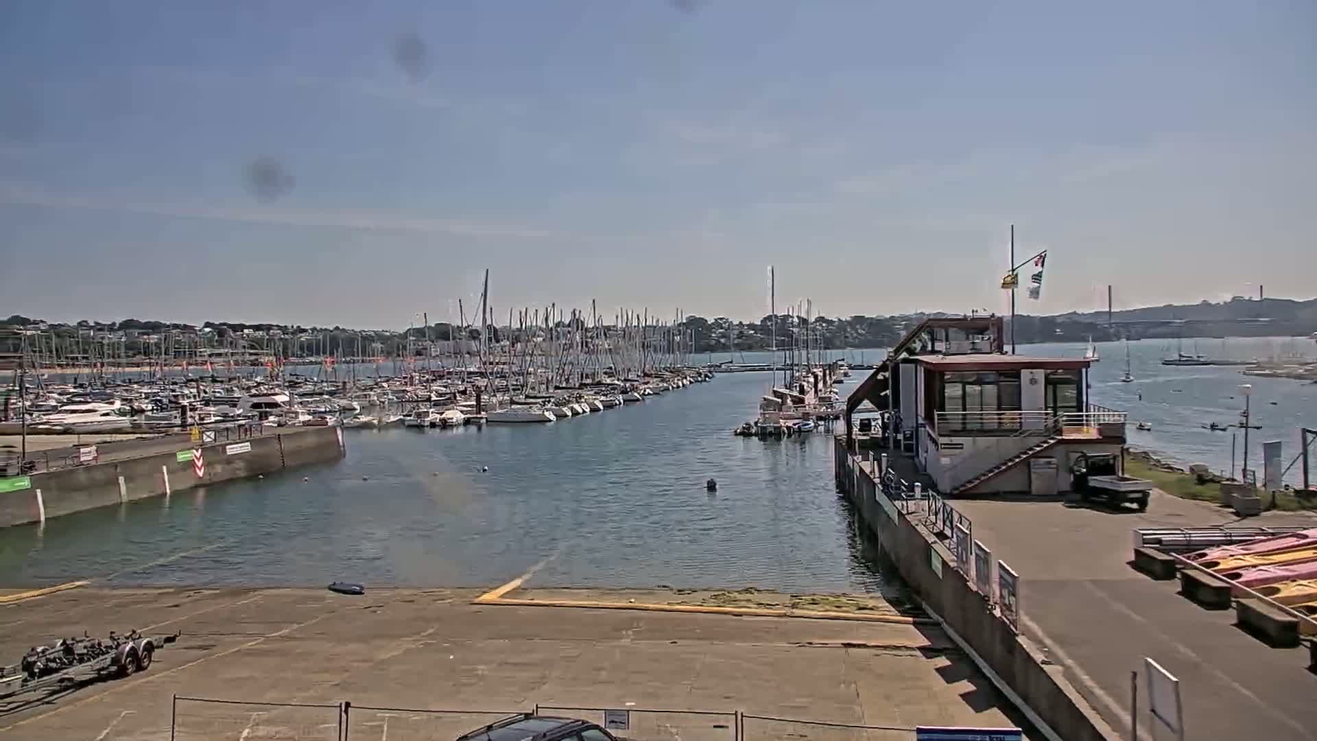 A marina filled with sailboats on a sunny day, with a small building and slipway in the foreground.
