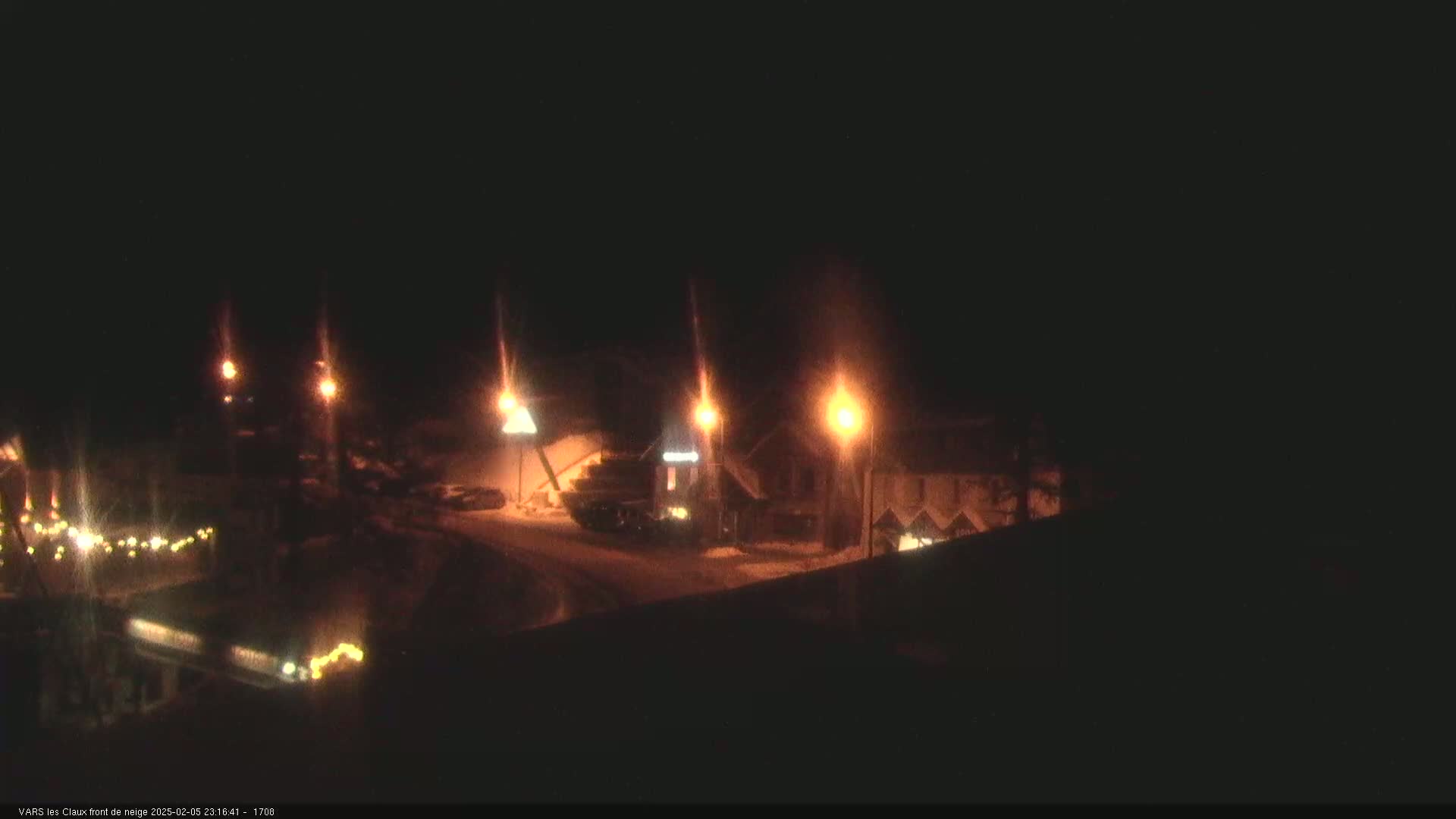 A snow-covered nighttime scene shows a few buildings illuminated by streetlights.