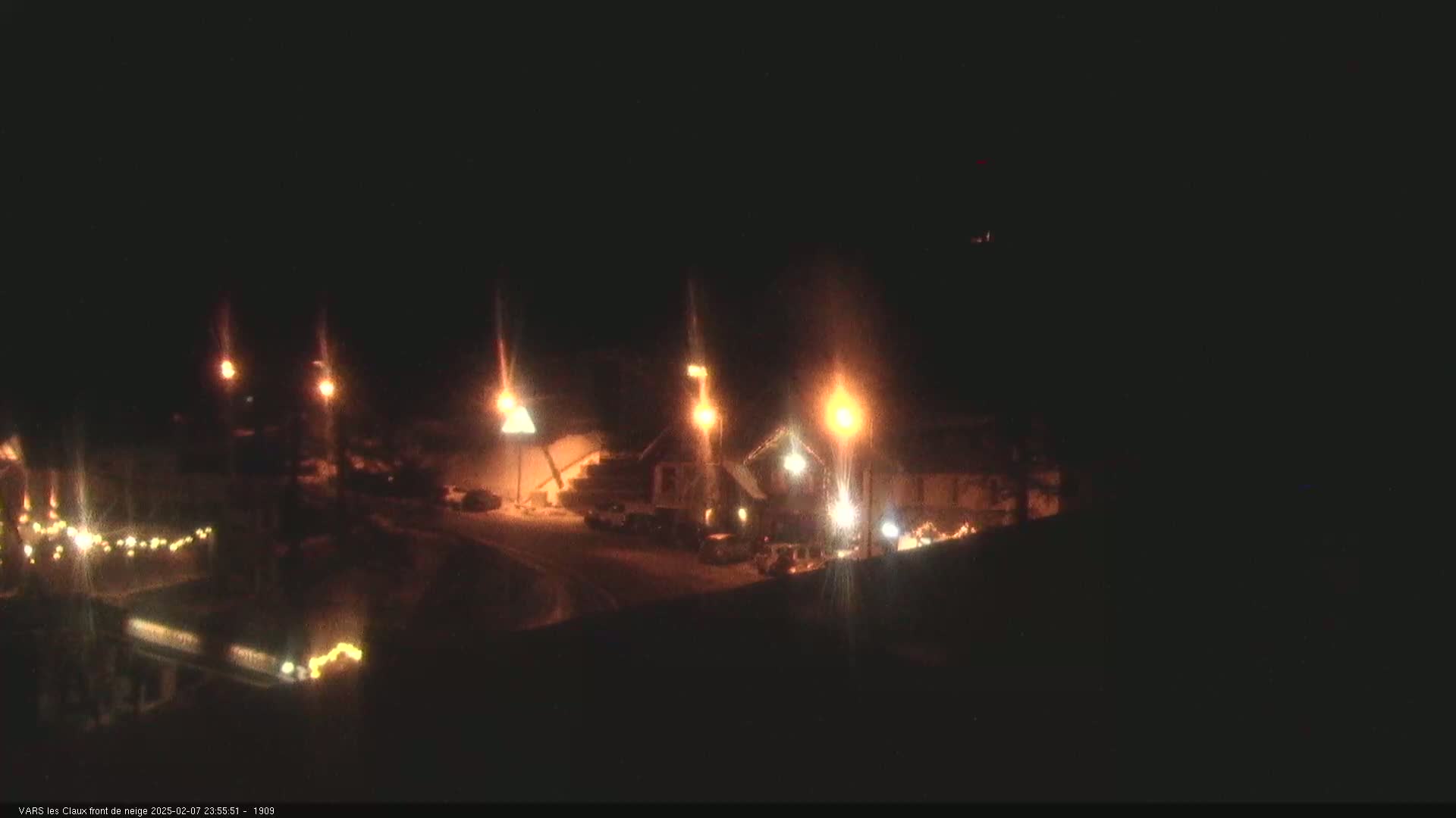 A nighttime view of a snow-covered area with several buildings illuminated by streetlights.