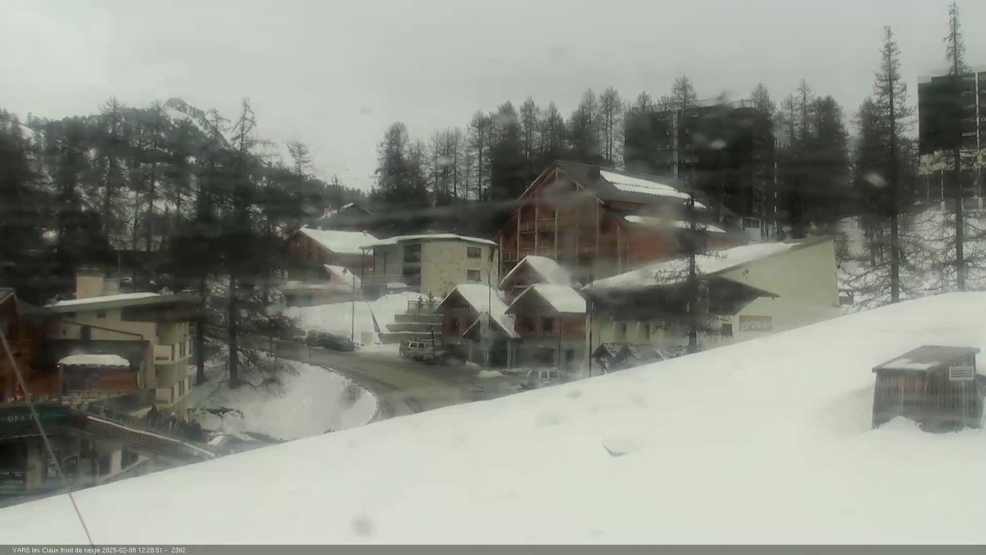 A snow-covered village nestled among dark evergreen trees in overcast conditions.