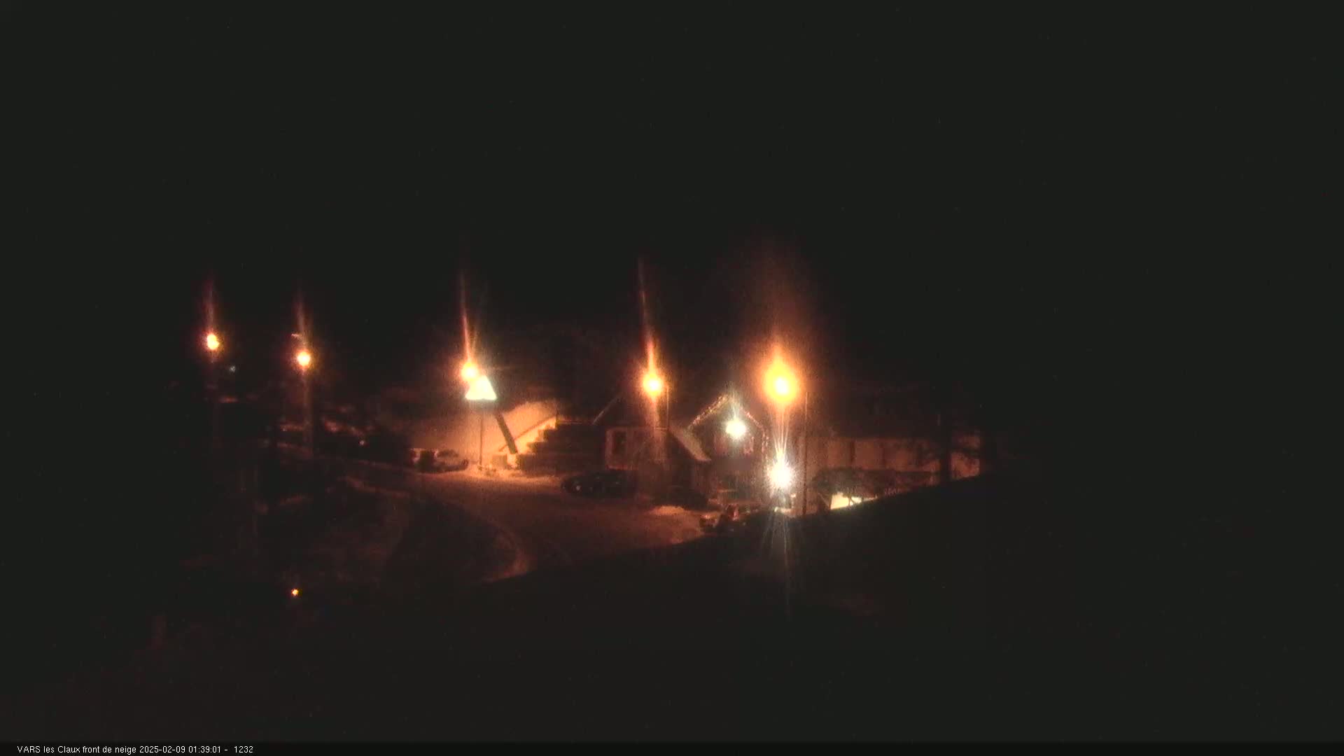 A nighttime view of a snow-covered area with several buildings illuminated by streetlights.