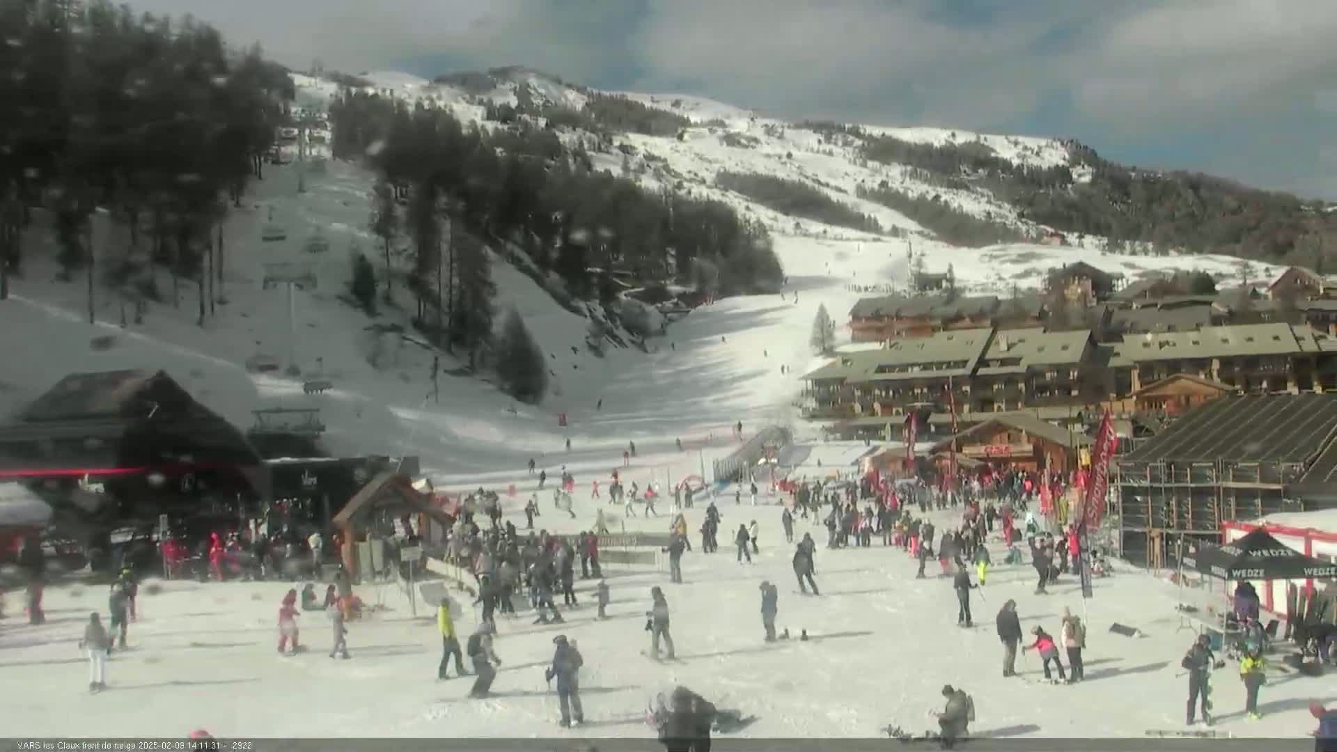A snowy mountainside ski resort with many skiers and snowboarders at the base on a bright, sunny day.