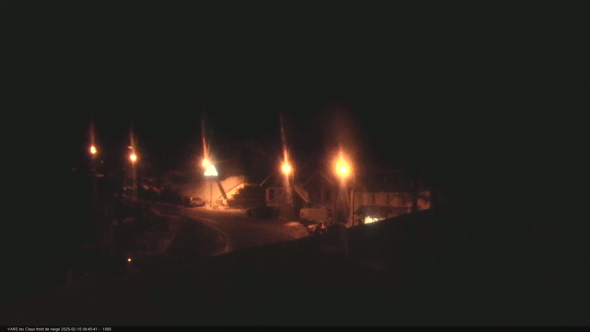 At night, several illuminated structures are visible in a snowy area, lit by streetlights.