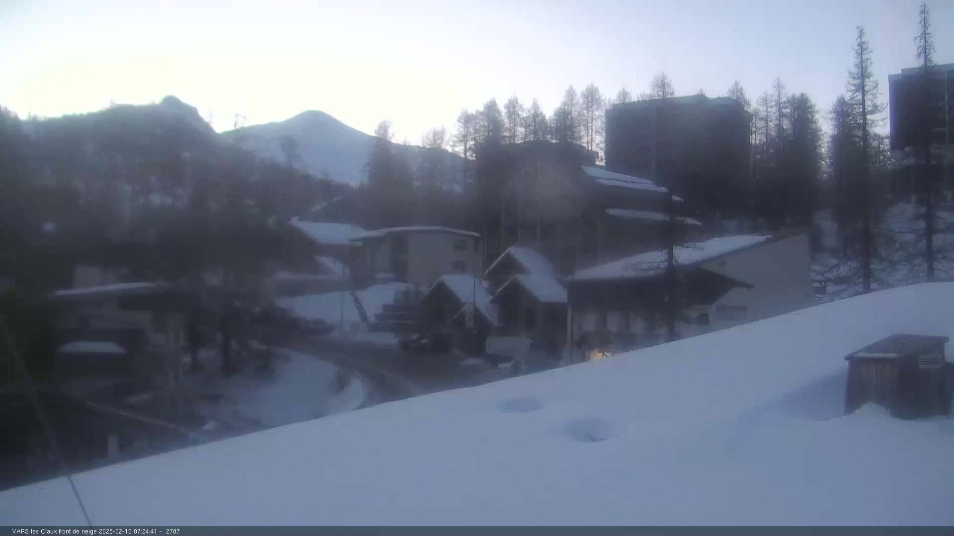 A snow-covered village nestled in a mountain valley under a hazy, twilight sky.