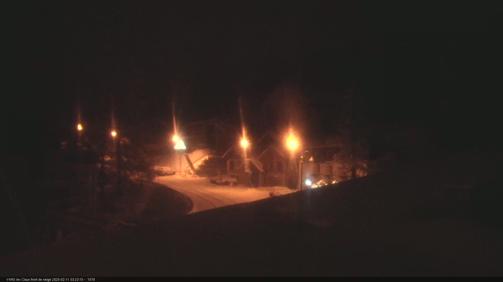 A nighttime, snowy scene shows a cluster of buildings lit by streetlights.