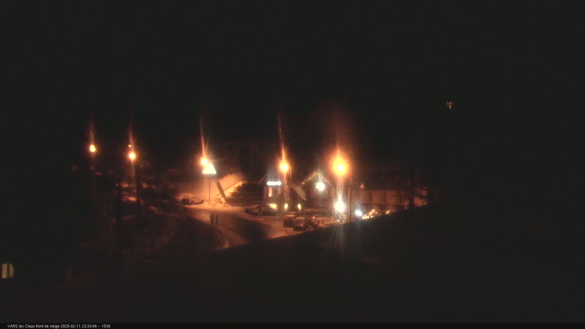 A nighttime view of a snow-covered area with several illuminated buildings and streetlights.