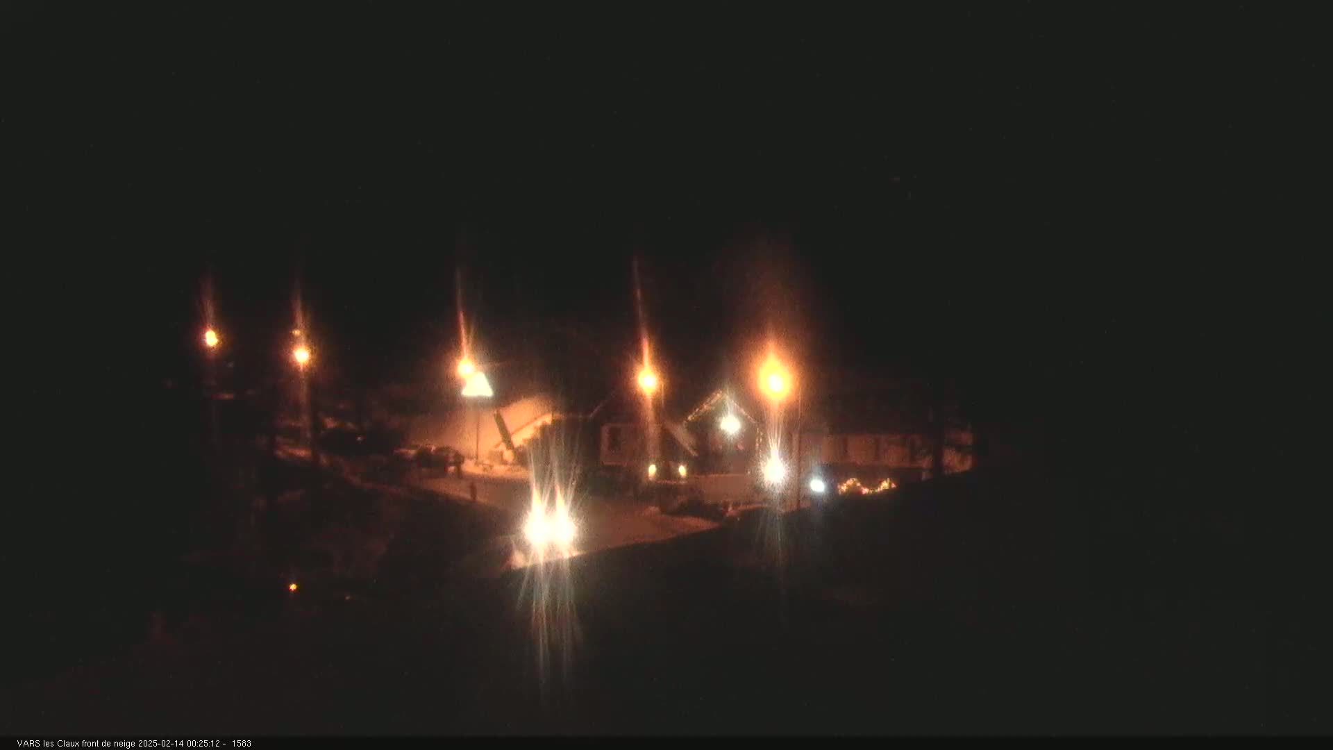 A nighttime, snow-covered scene shows several buildings illuminated by streetlights.