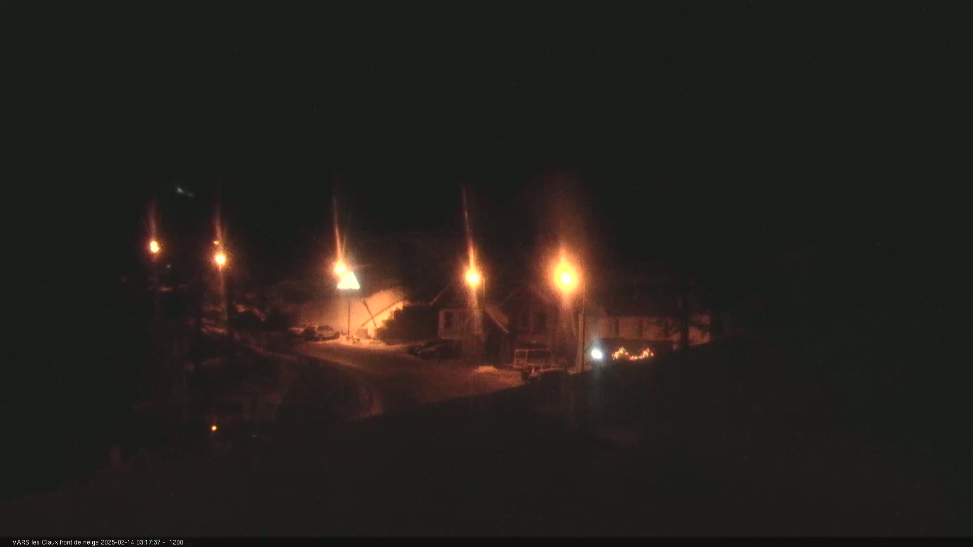A nighttime, snow-covered scene shows several illuminated buildings and streetlights.