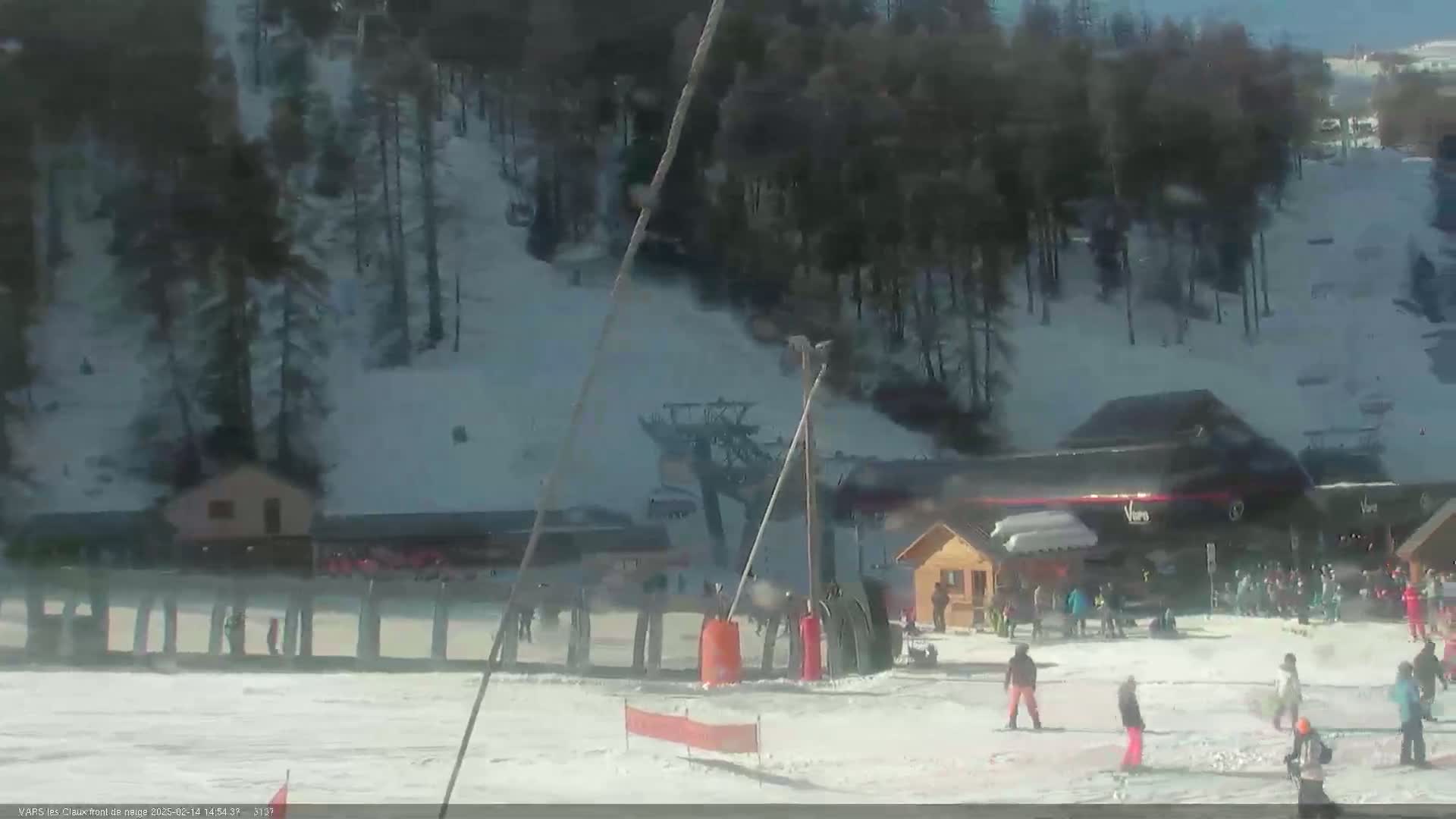 A snow-covered ski slope with several skiers and snowboarders near the base of a ski lift on a sunny day.