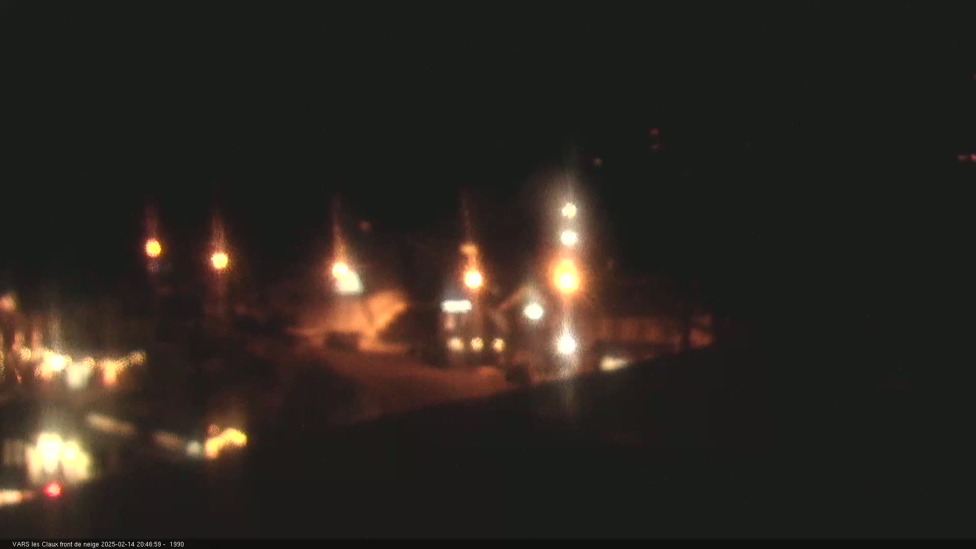 A nighttime, blurry view of an area with several lights, possibly a parking lot or road, illuminated by streetlights and vehicle headlights.