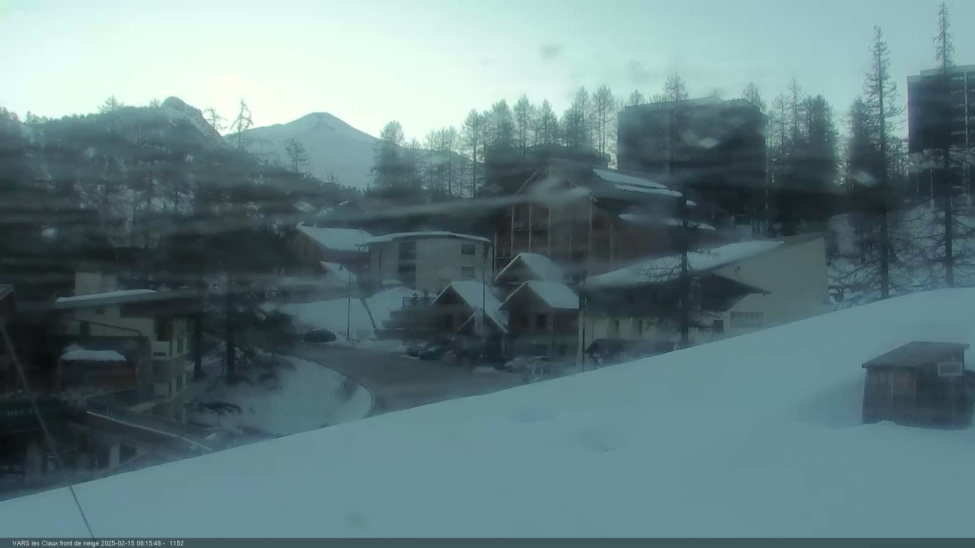 A snow-covered village nestled in a mountainous area, with a hazy, overcast sky.