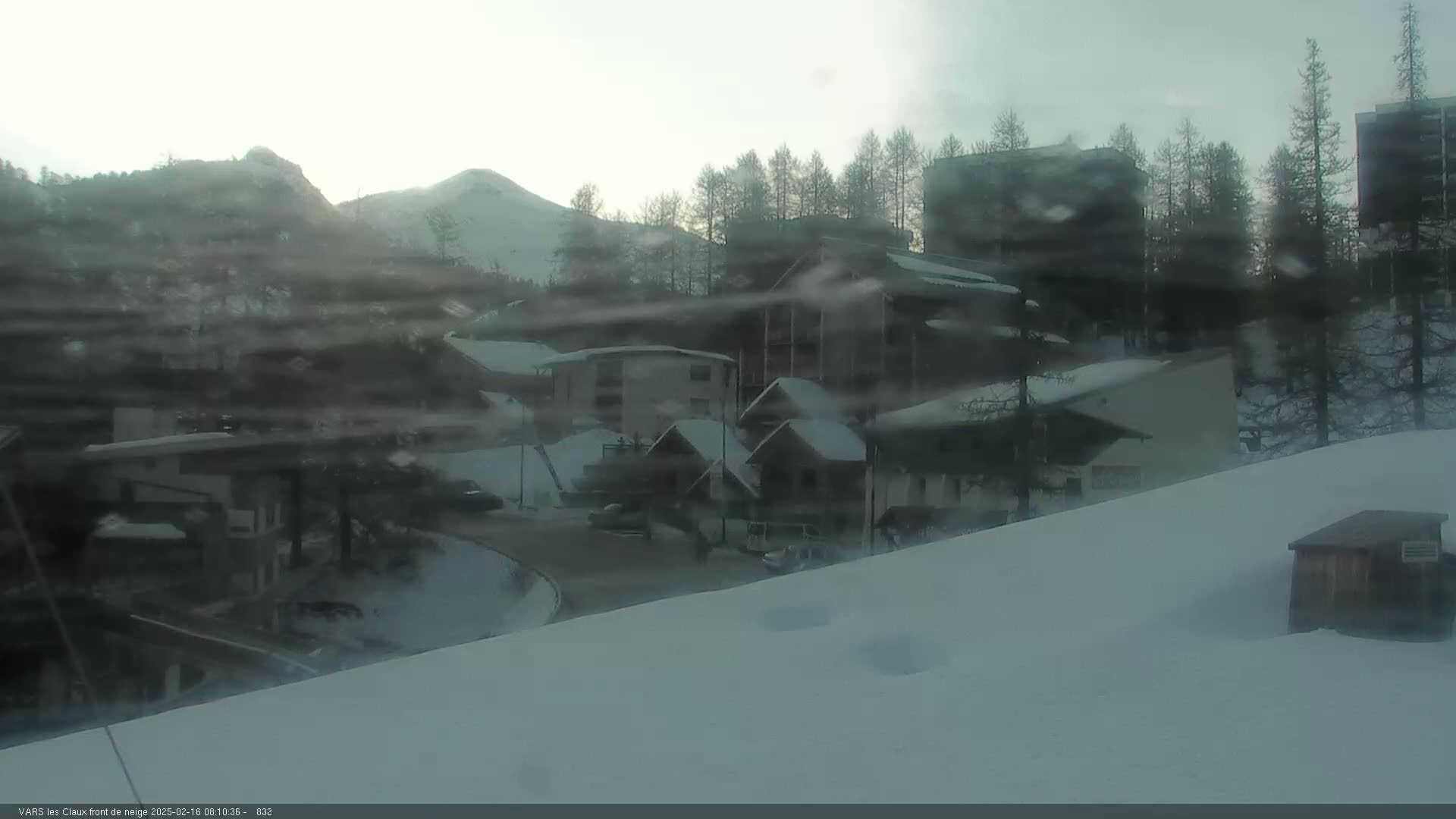 A snow-covered village nestled in a mountainous region under a hazy, overcast sky.