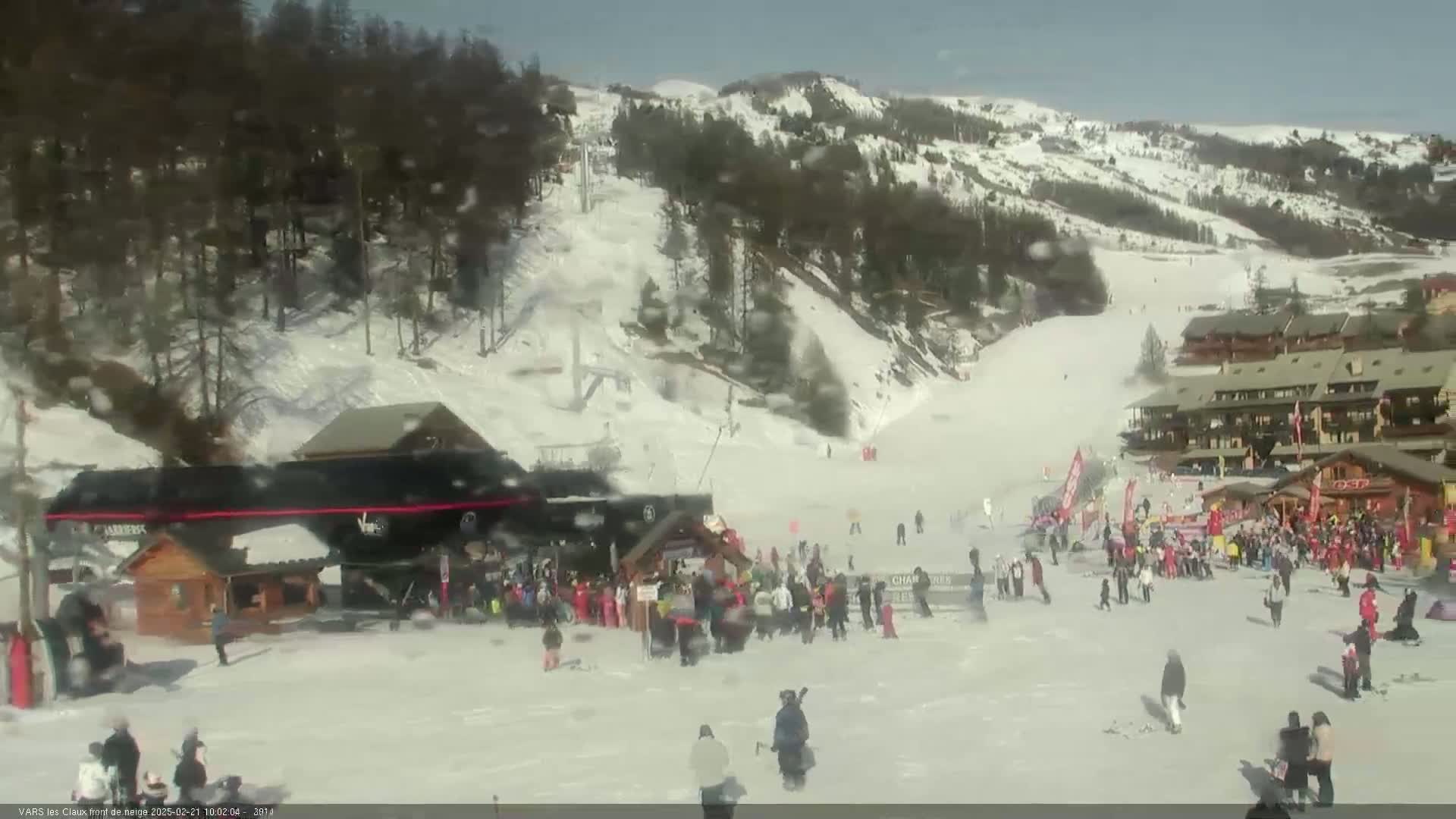 A snowy ski resort on a sunny day with many people gathered near the base of a ski lift.