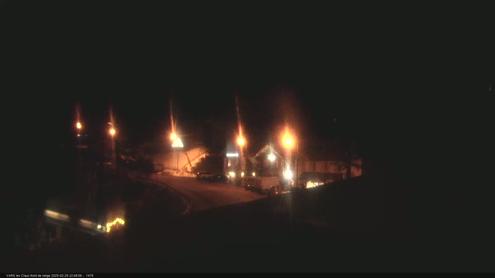 A nighttime scene shows a snow-covered road and buildings illuminated by streetlights.