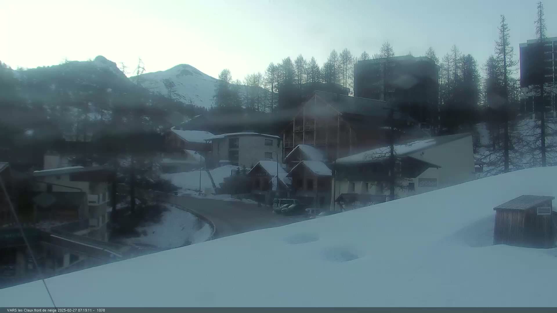 A snow-covered village nestled in a mountainous region under an overcast sky.