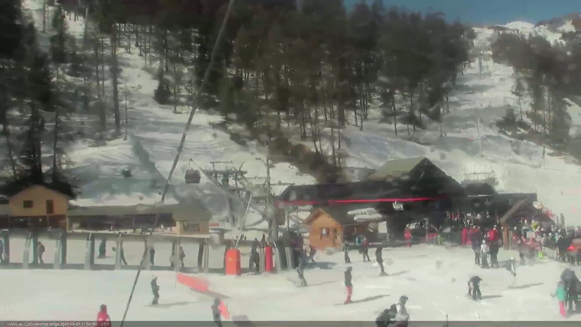 A ski resort on a sunny day with skiers and snowboarders at the base of a snow-covered hill.