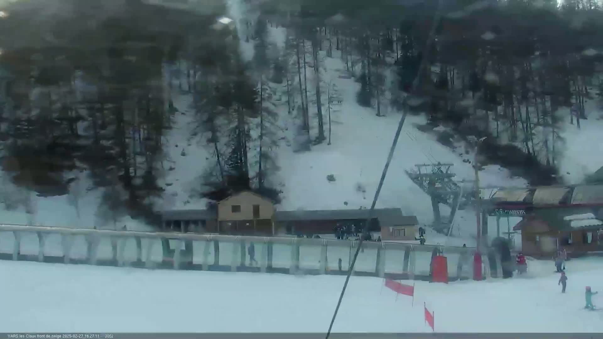 A snowy ski slope with a chairlift, several small buildings, and a few skiers is visible from a high vantage point.