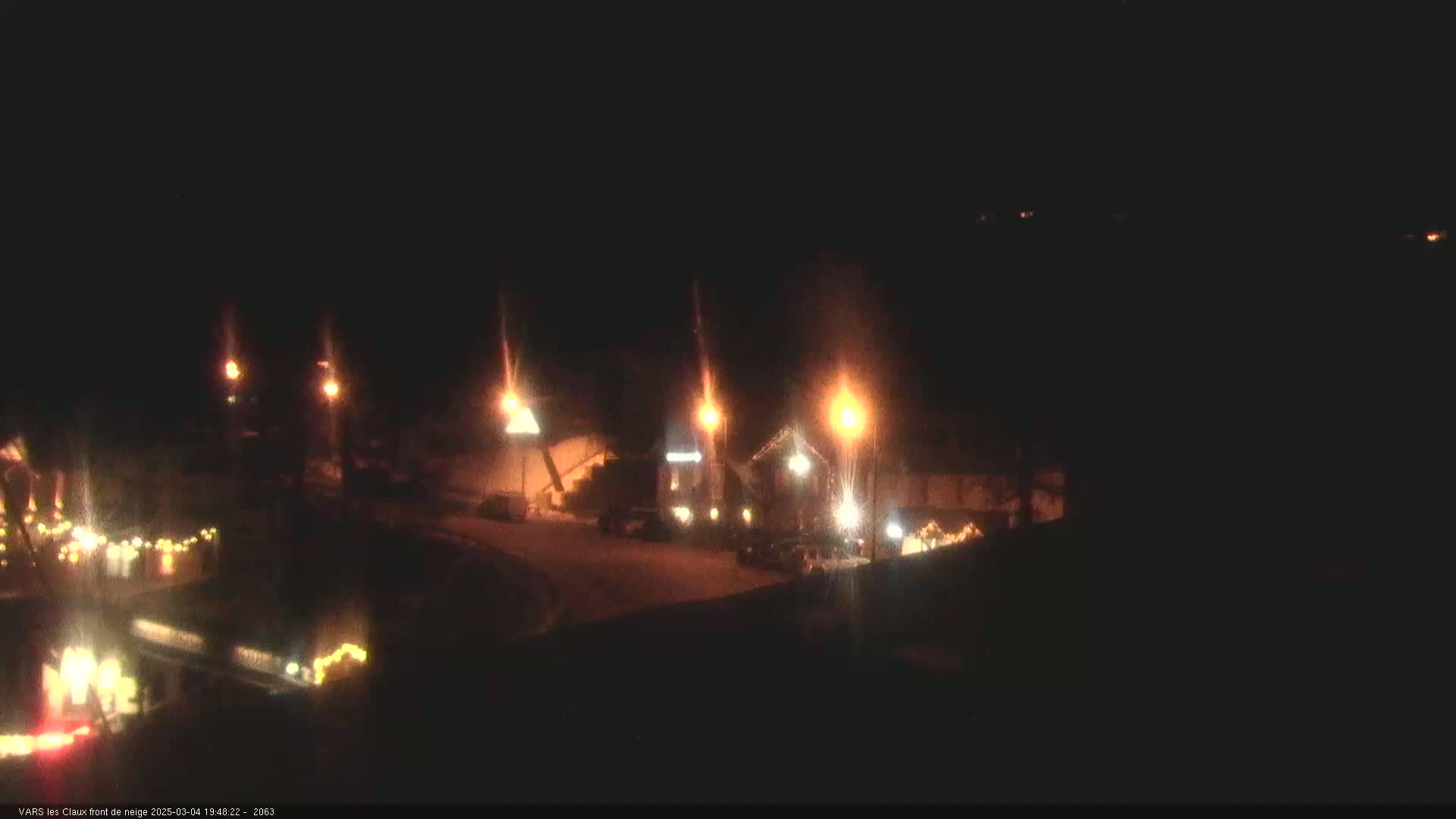 A nighttime, snowy scene shows several illuminated buildings and streetlights.