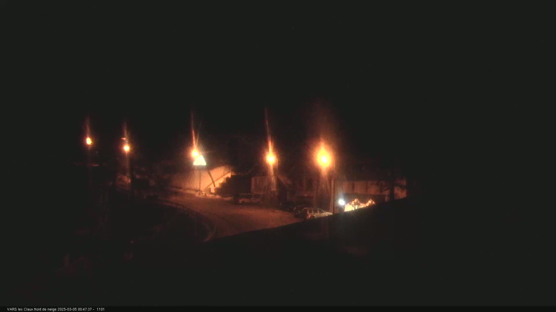 At night, several streetlights illuminate a dark road and buildings.
