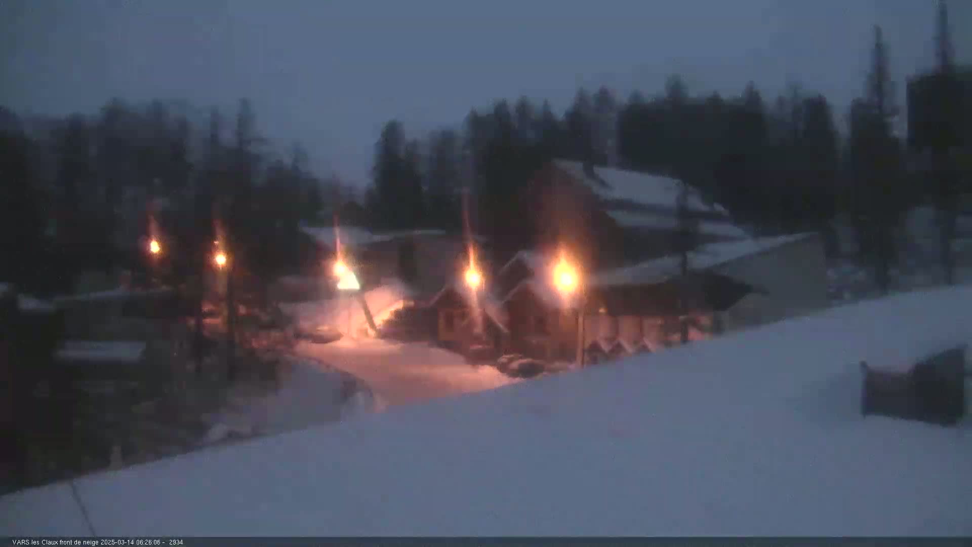 Snow-covered buildings are illuminated by several bright lights at night.