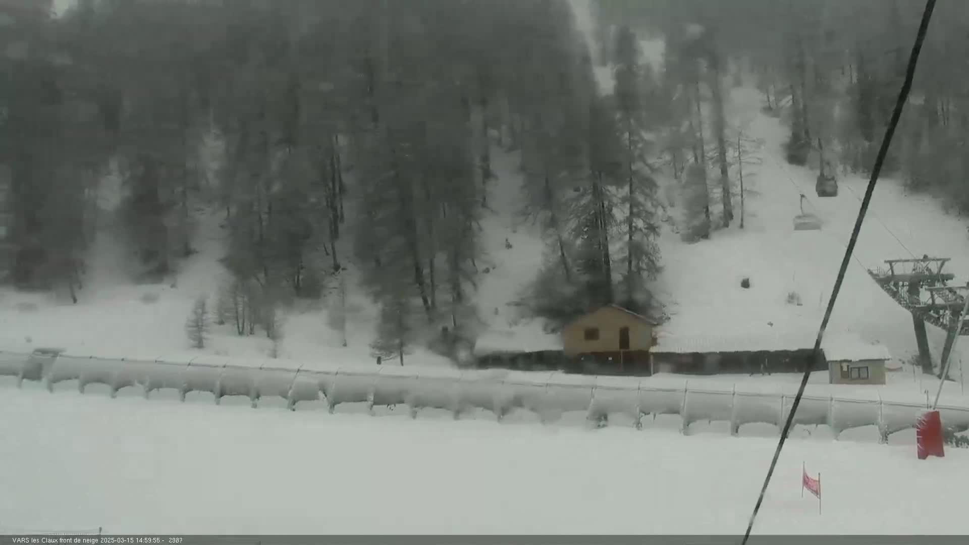 A snow-covered ski slope with a small building and chairlift in the background during a snowstorm.